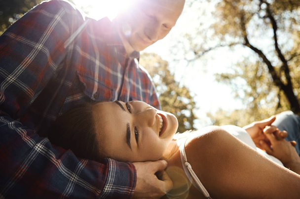 Een jong romantisch stel dat verliefd is, brengt tijd door in het park. jonge vrouw liggend op knieën van de man en glimlachen met zonnestralen achtergrond. - Foto, afbeelding
