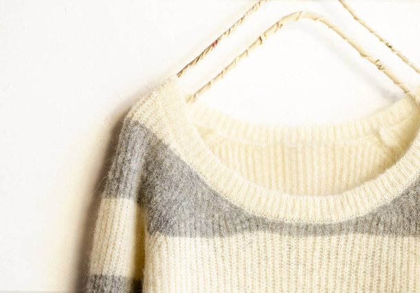 White and gray striped sweater hanging on clothes hanger on white background. - 写真・画像