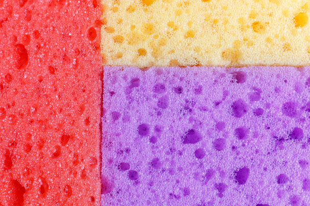 Цветные губки для мытья посуды и других бытовых нужд. Вид сверху. Текстура красного, фиолетового и оранжевого губок разбросаны в трети, пена резины
. - Фото, изображение