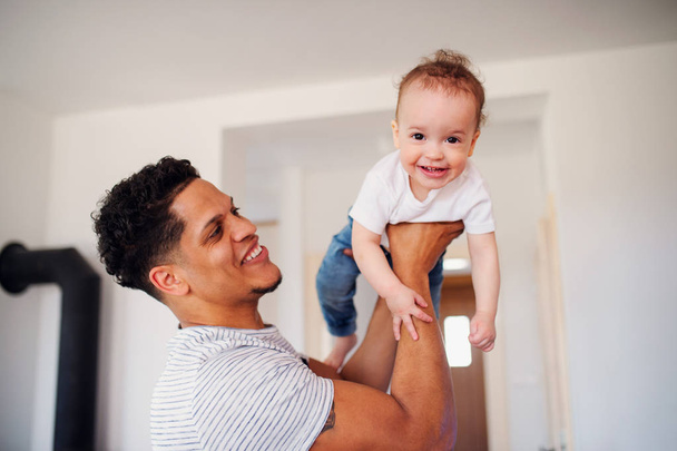 A portrait of father and small toddler son indoors at home, playing. - Foto, imagen