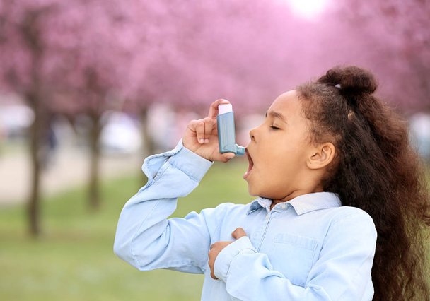 吸入器を持つアフリカ系アメリカ人の女の子は、春の日に屋外で喘息発作を起こしました - 写真・画像