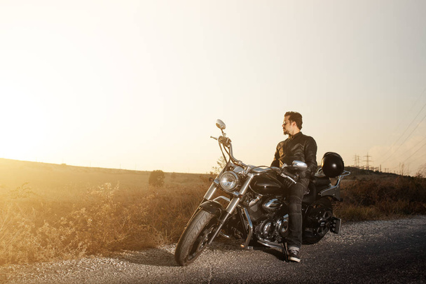 Side view of a young male  biker sitting on the side of the road against sunset while traveling by bike. - Φωτογραφία, εικόνα