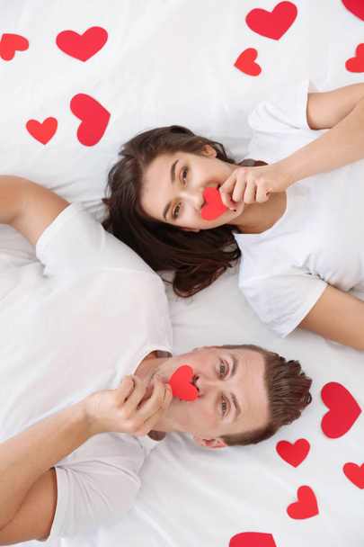 Щаслива молода пара з паперовими серцями лежить в ліжку
 - Фото, зображення