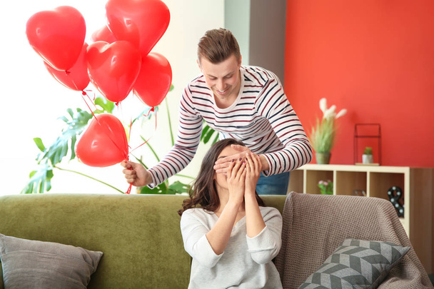 Young man greeting with heart shaped air balloons his wife at home - Fotoğraf, Görsel