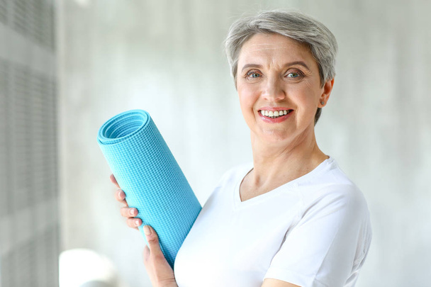 Sporty mature woman with yoga mat at home - Photo, Image
