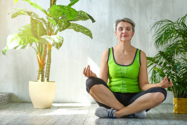 Спортивная зрелая женщина медитирует дома
 - Фото, изображение