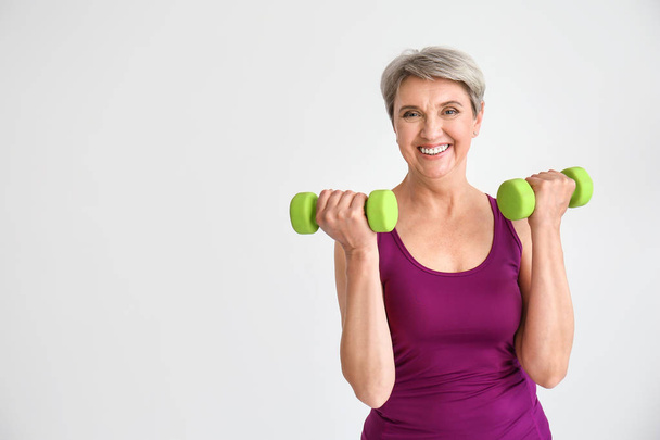 Sporty mature woman with dumbbells on light background - Foto, immagini