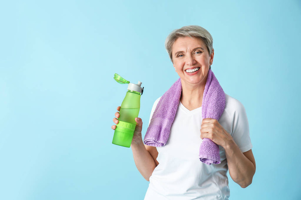 Sporty mature woman with towel and bottle of water on color background - Photo, Image