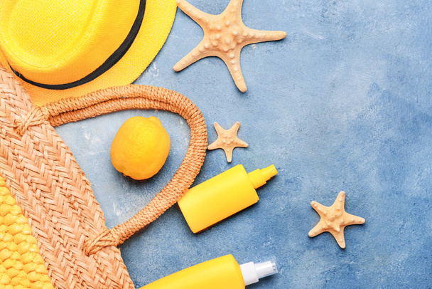 Beach bag with sun protection cream, lemon fruit and starfishes on color background - Foto, afbeelding