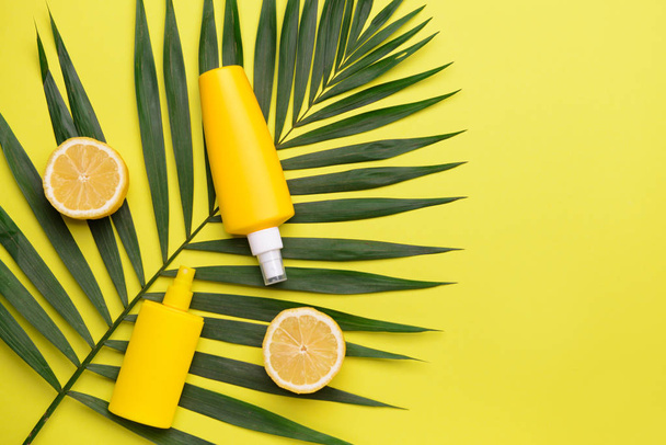 Sun protection cream with lemon fruit and tropical leaf on color background - Photo, Image