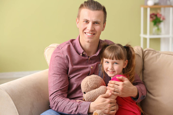 Happy man with little adopted girl sitting on sofa at home - Foto, afbeelding