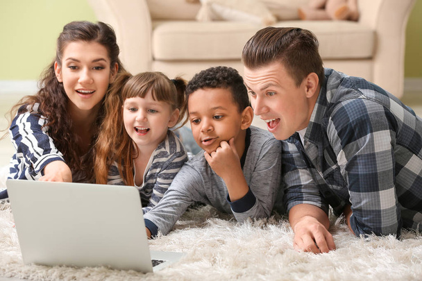 Szczęśliwa para z małymi adoptowanych dzieci za pomocą laptopa w domu - Zdjęcie, obraz