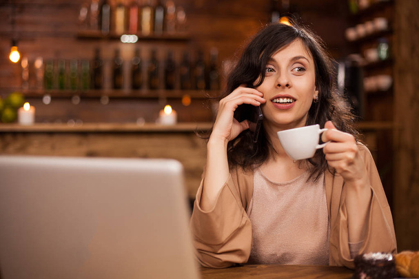 Retrato de una mujer de negocios moderna en una cafetería hipster hablando por teléfono y sosteniendo una taza de café
 - Foto, imagen