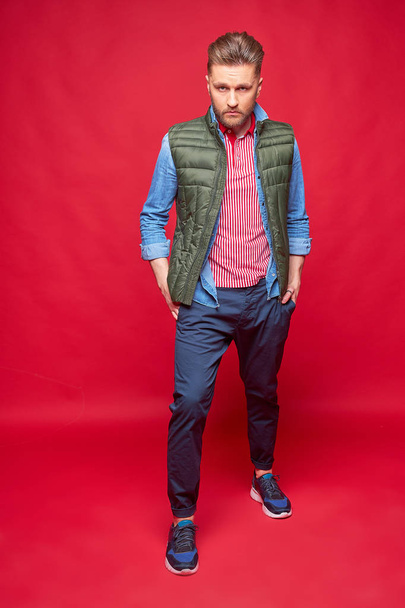 Male model posing in casual clothes. Fashion portrait, studio shot, red background - Photo, Image