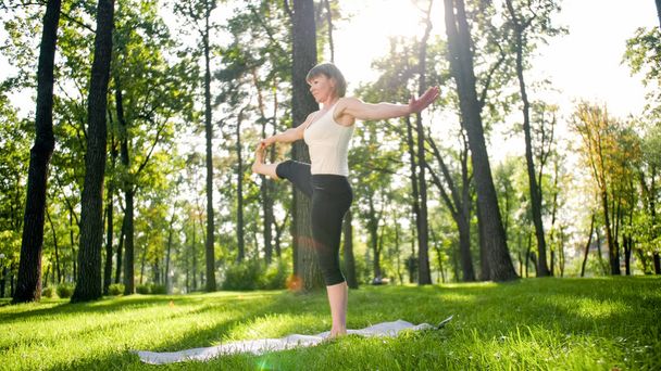 Zdjęcie uśmiechniętej kobiety robi jogi i ćwiczeń fitness. Ludzie w średnim wieku dbają o swoje zdrowie. Harmonia ciała i umysłu w przyrodzie - Zdjęcie, obraz