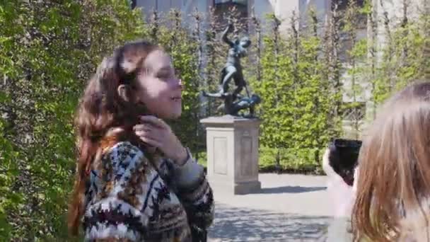 zwei junge Frauen, die im Park zwischen dekorativen Pflanzen spazieren und Fotos mit Statuen machen - Filmmaterial, Video