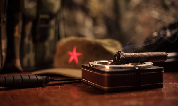 Close-up van een Cubaanse sigaar en asbak op de houten tafel. Communistische dictator Commander tabel in donkere kamer. Het werktafel concept van Army General. - Foto, afbeelding