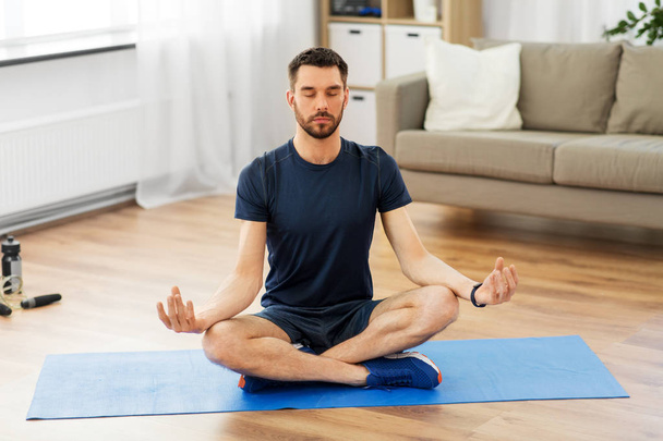 man meditating in lotus pose on yoga mat at home - Foto, Imagem