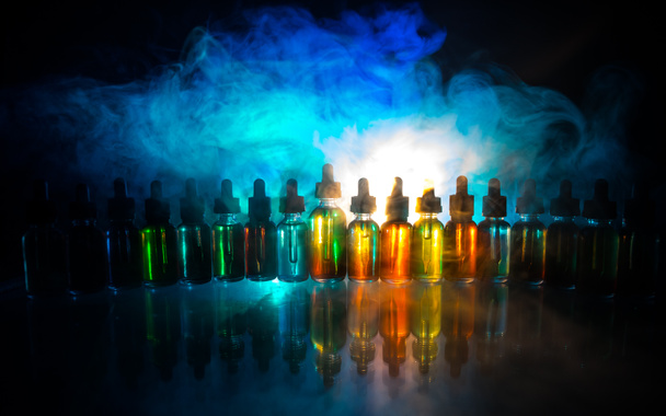 Vape concept. Smoke clouds and vape liquid bottles on dark background. Light effects. Useful as background or electronic cigarette advertisement. - Photo, Image