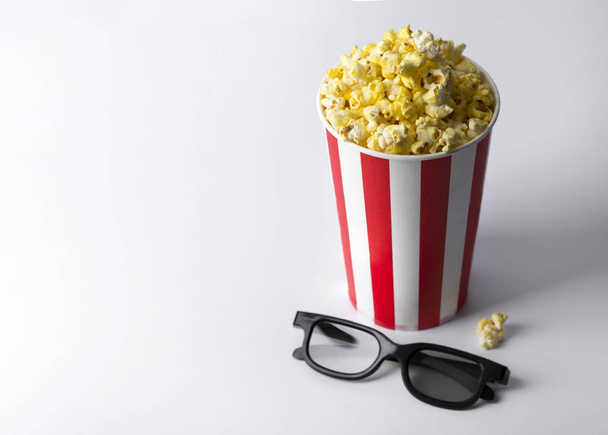 Popcorn im gestreiften roten Eimer mit 3D-Gläsern am weißen Tisch. - Foto, Bild
