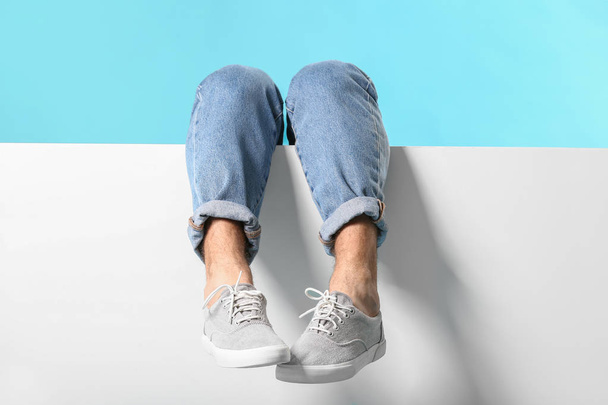 Legs of young man in jeans and blank poster on color background - Valokuva, kuva
