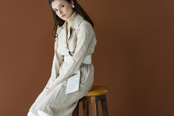 fashionable woman sitting on chair isolated on brown, looking at camera - Foto, Imagem