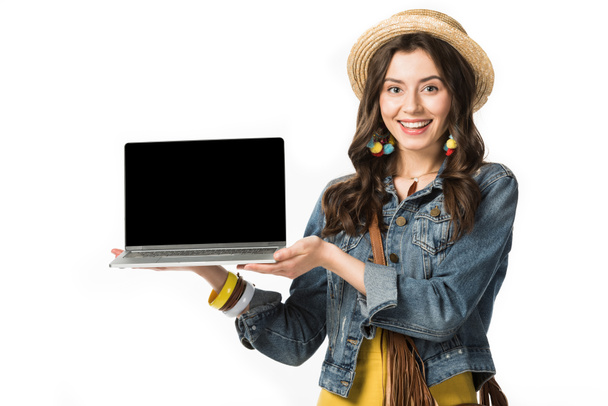 cheerful boho girl in boater holding laptop with blank screen isolated on white - 写真・画像