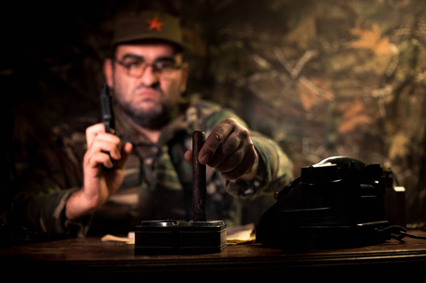 Zlý diktátor sedí na stole. Rozzlobený komunistický generál sedící na mysu nebo kubánský velitel v temném pokoji. - Fotografie, Obrázek