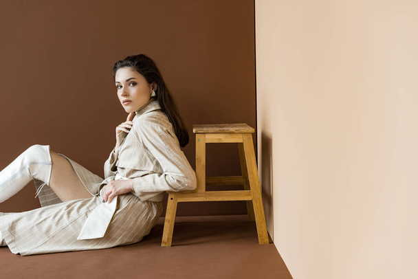 fashionable model in trench coat and white boots sitting on floor, looking at camera - Foto, Imagen
