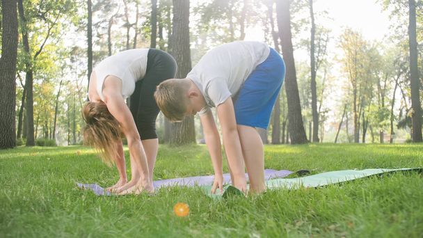 Bild einer Frau mittleren Alters, die einem Jungen Yoga und Fitness im Park beibringt. Familie kümmert sich um ihre Gesundheit - Foto, Bild