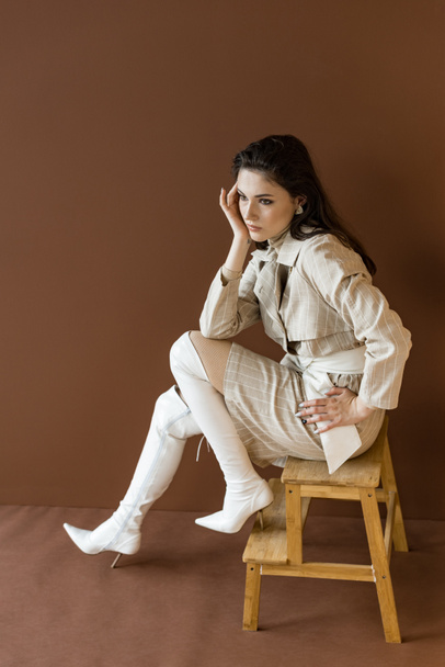 high angle view of trendy model in stylish trench coat looking away, sitting on stairs - Фото, изображение