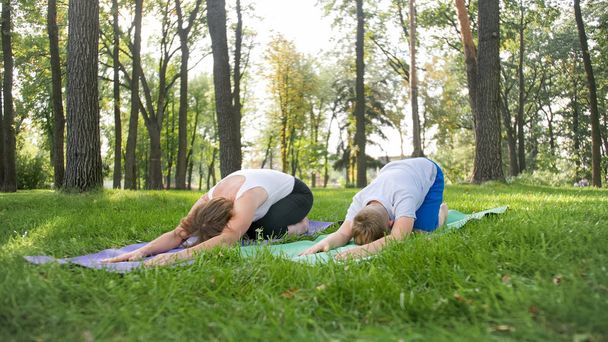 Retrato de un niño de 12 años haciendo ejercicio de yoga con su madre en el parque. Meditación y estiramiento familiar en el bosque
 - Foto, Imagen