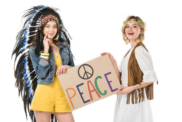 dos chicas hippies bisexuales sonrientes en tocado indio y guirnalda sosteniendo pancarta con inscripción aislada en blanco
 - Foto, imagen