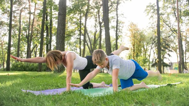 Image of middle aged woman teaching teenage boy doing yoga and fitness on grass at park. Family taking care of their health - Zdjęcie, obraz
