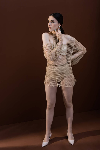 beautiful woman in mesh dress standing on brown background, looking away - Valokuva, kuva