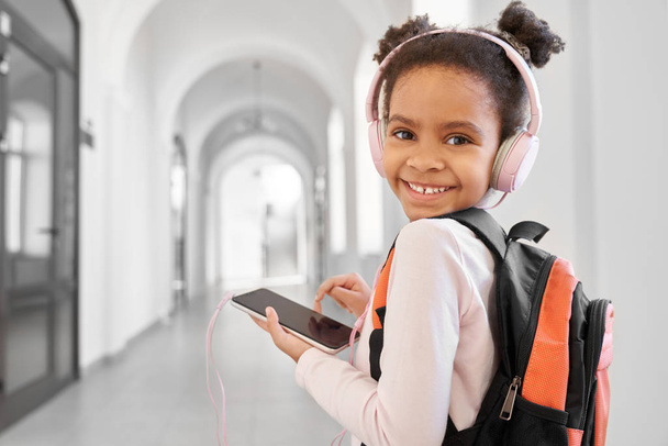 Sevimli çocuk okulda sırt çantası ve kulaklık ile poz. - Fotoğraf, Görsel