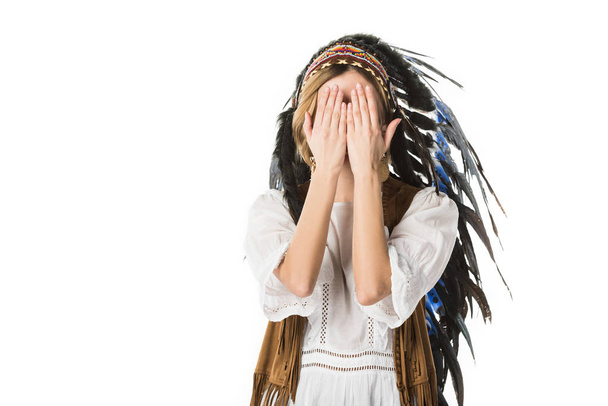 young woman in indian headdress covering face with hands isolated on white - Photo, Image
