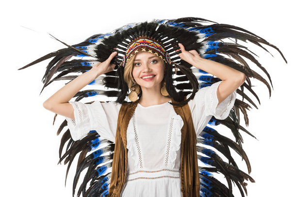smiling boho girl in indian headdress looking at camera isolated on white - Фото, изображение