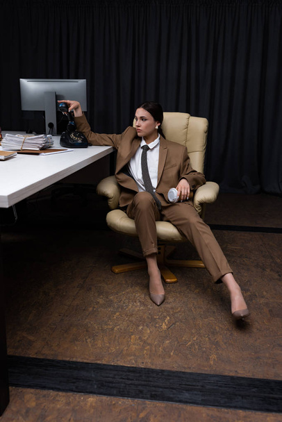 красива бізнес-леді з гарнітурою і паперовою чашкою сидить на кріслі в офісі, дивлячись
 - Фото, зображення