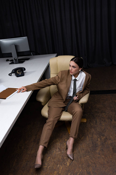 high angle view of businesswoman in formal wear sitting on armchair in office, looking away - Photo, Image