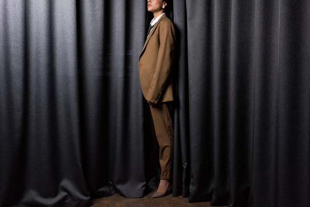 side view of fashionable model in suit standing in studio with grey curtain background - Photo, Image