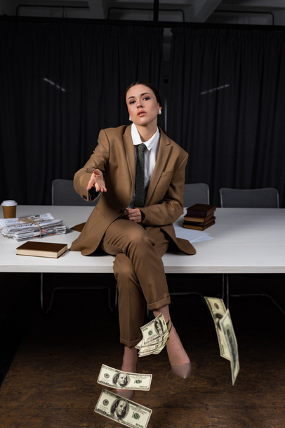masada oturan yetişkin iş kadını, bacak larını geçerek, kameraya bakmak ve para atma - Fotoğraf, Görsel