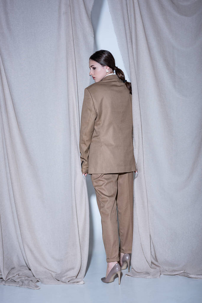 back view of fashionable model in suit standing on light grey curtain background - Valokuva, kuva