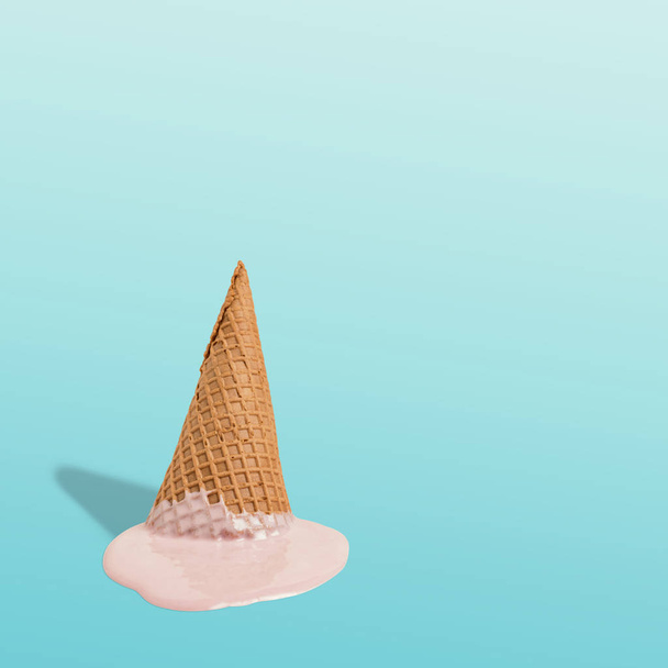 Melted ice cream with ice cream cone on pastel blue background. Minimal summer food concept.  - Фото, изображение
