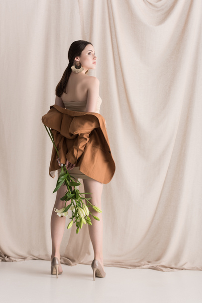 fashionable model standing on curtain background, holding flowers in hands - Fotó, kép