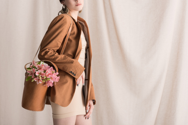 cropped view of stylish woman carries flowers in bag, standing on curtain background - Foto, afbeelding