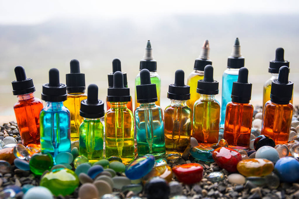 Vape concept. Beautiful colorful vape liquid glass bottles outdoor on stones. Useful as background or electronic cigarette advertisement. - Photo, Image