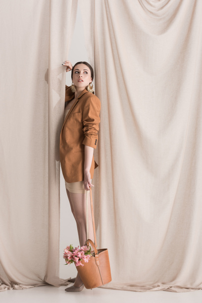 vista lateral del modelo de moda llevando flores en el bolso de pie sobre el fondo de la cortina
 - Foto, imagen