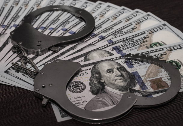 one hundred dollar bills and steel handcuffs close up - Фото, зображення