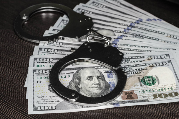one hundred dollar bills and steel handcuffs close up - Foto, afbeelding